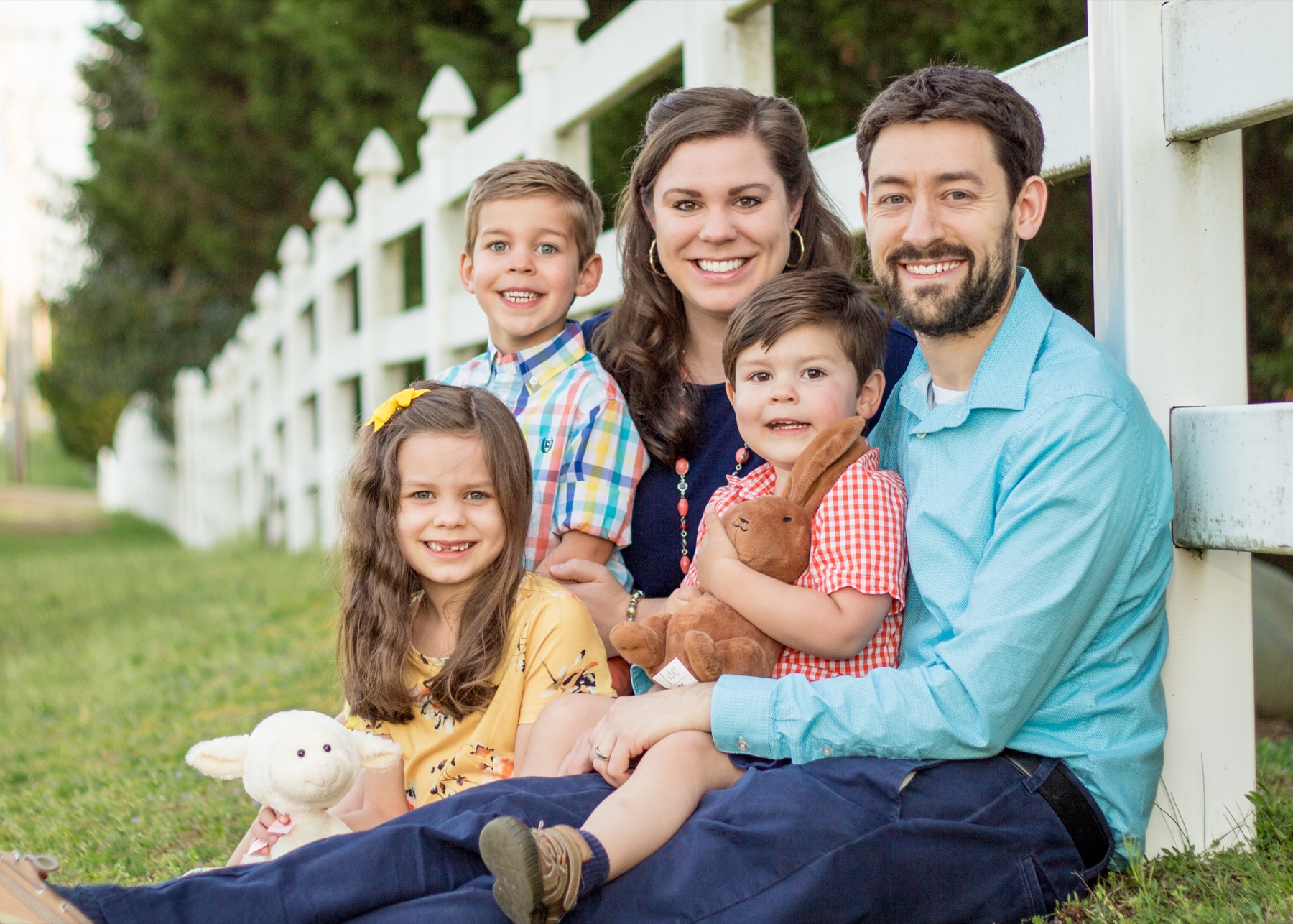 Family of five seated together by a white fence
