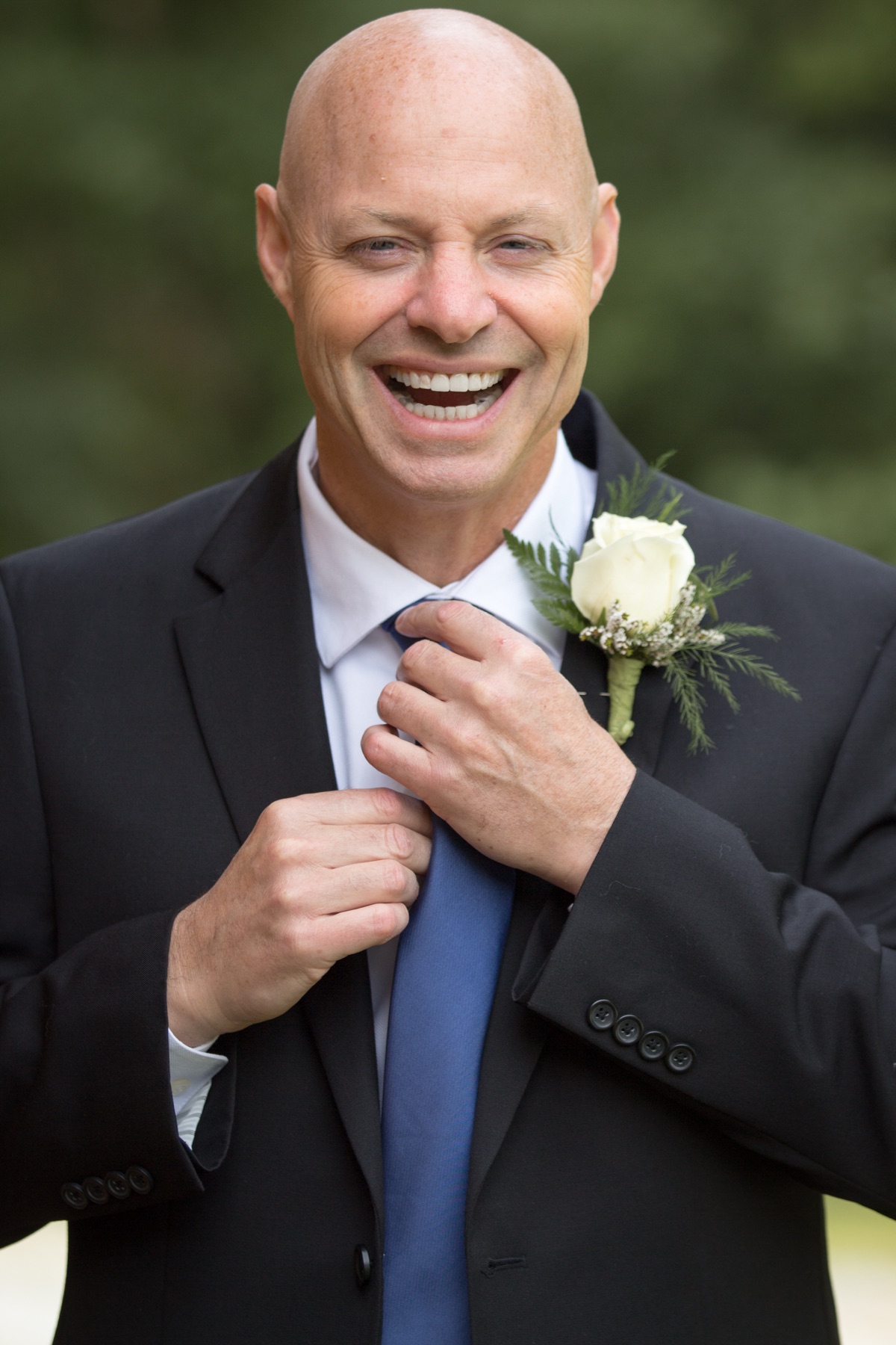 Groom adjusting his tie with a white rose boutonniere