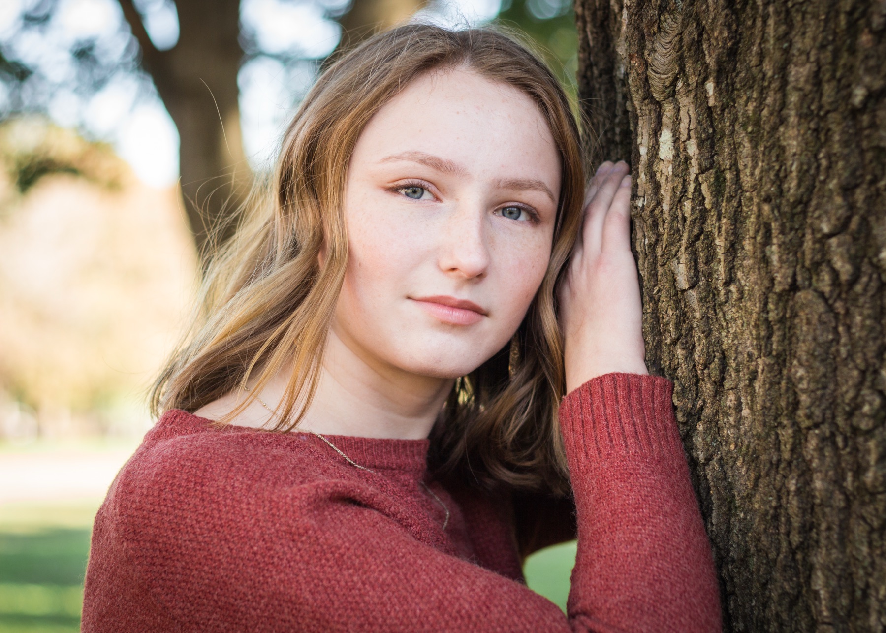 Senior portrait of a young woman leaning against an oak tree